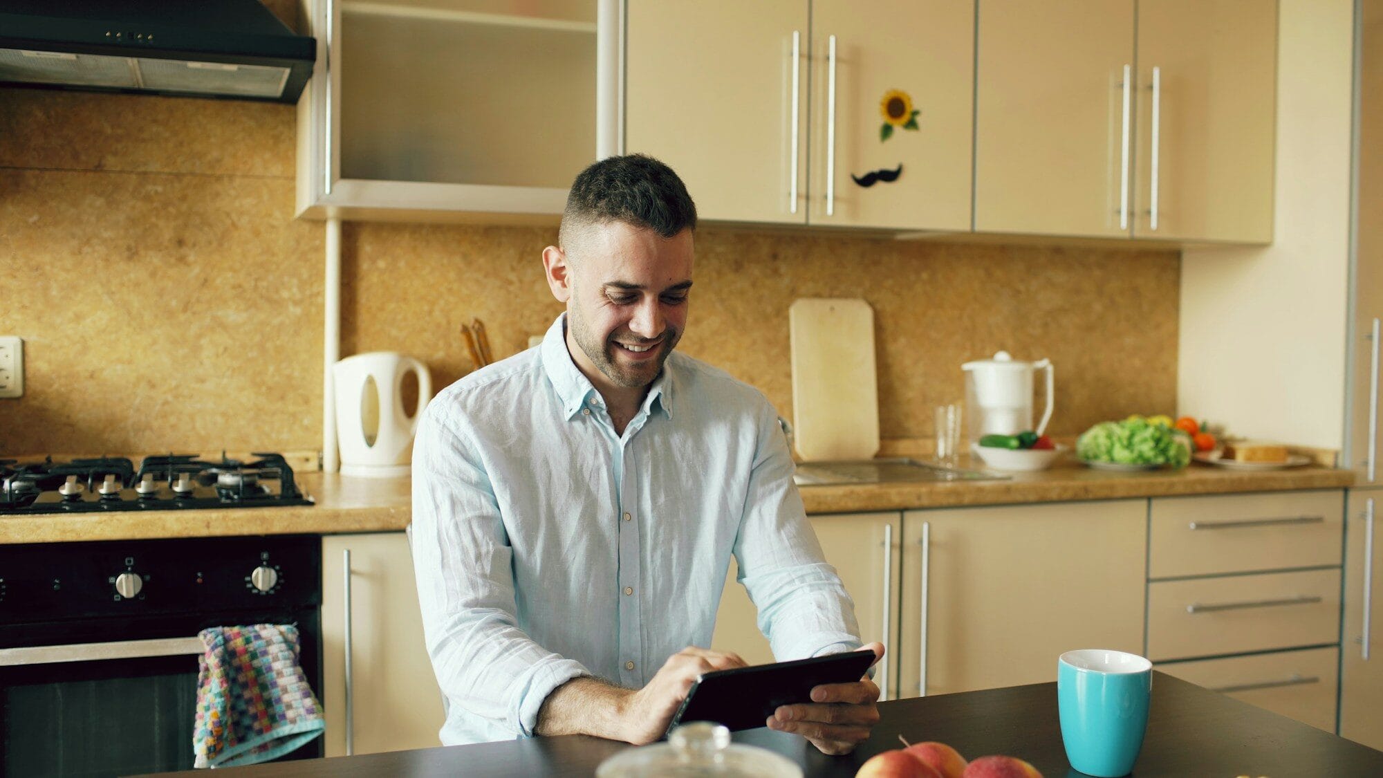 Man smiling while using a tablet in the kitchen.